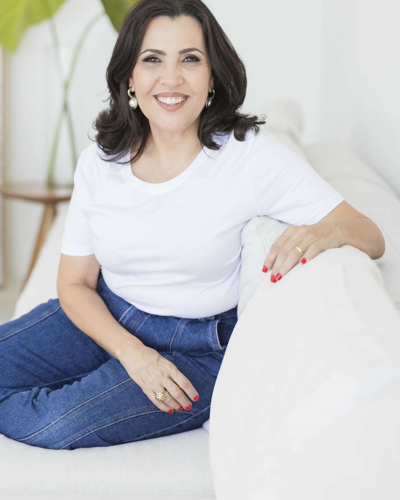Tatiana Teixeira, de camiseta branca, sentada em um sofá claro